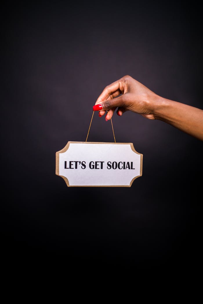 Close-up of a hand holding a sign with Lets Get Social on a dark background.